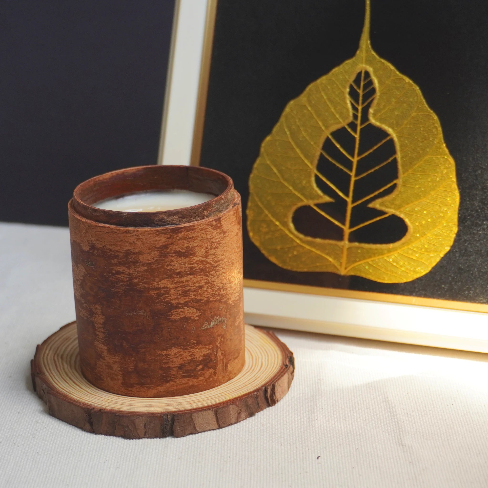 Wooden candle holder with a lit candle on a wooden coaster, with a leaf design in the background, use for relax and meditation