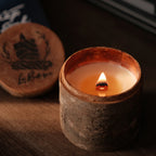 Candle in a rustic container with a wooden lid featuring branding on a dark background
