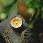 Youthful Joy cented candle in a decorative holder on a wooden surface with greenery in the background