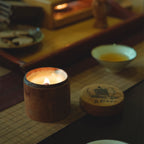 Candle with aroma essential oils in a cinnamon wooden holder on a table with a bowl of tea and a coaster.